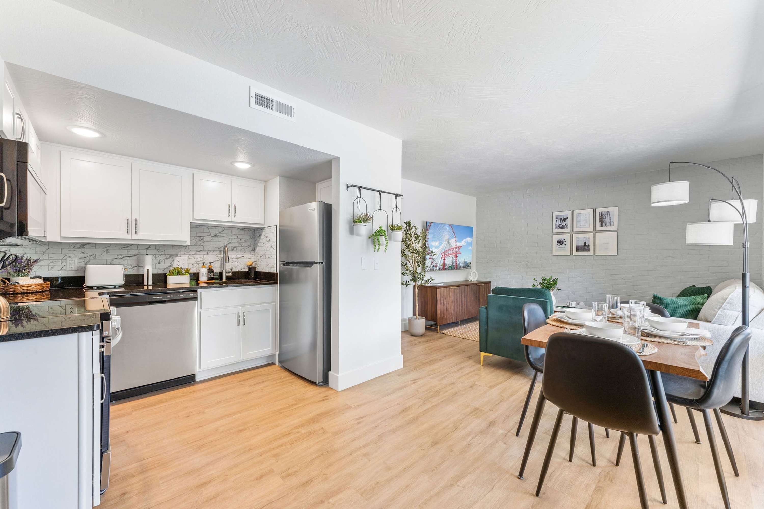 A modern kitchen with white cabinets, a stainless steel refrigerator, and a dining area with a wooden table and chairs.