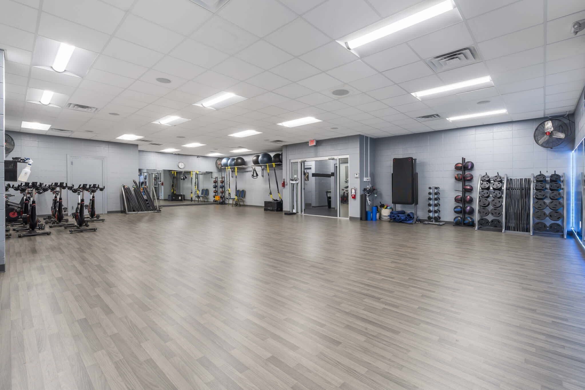 Un gimnasio amplio con diversos equipos de ejercicio, un espejo grande y un reloj en la pared.