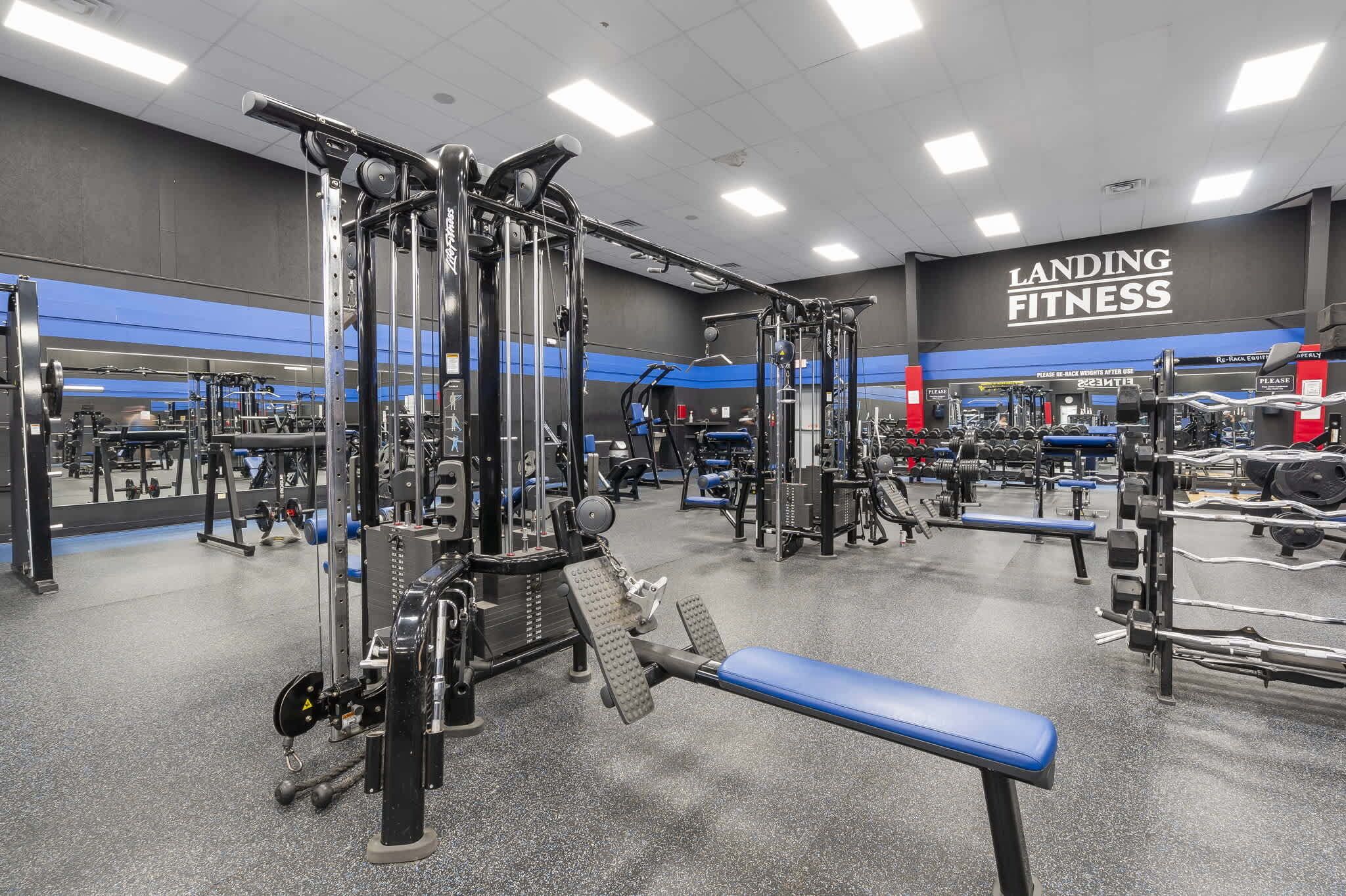 Un gimnasio con diferentes equipos de ejercicio, bancos y un espejo grande.