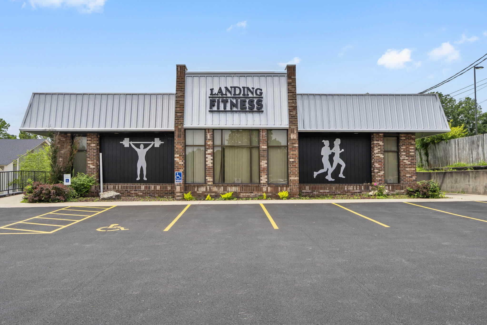 A building with a sign reading "Landing Fitness" and a parking lot in front.
