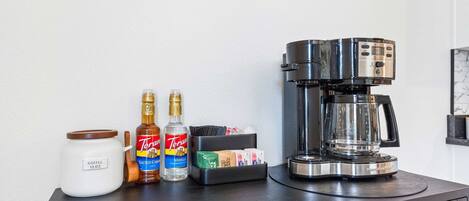 Una estación de café con una cafetera, un tarro de café y botellas de sirope Torani y extracto de vainilla.