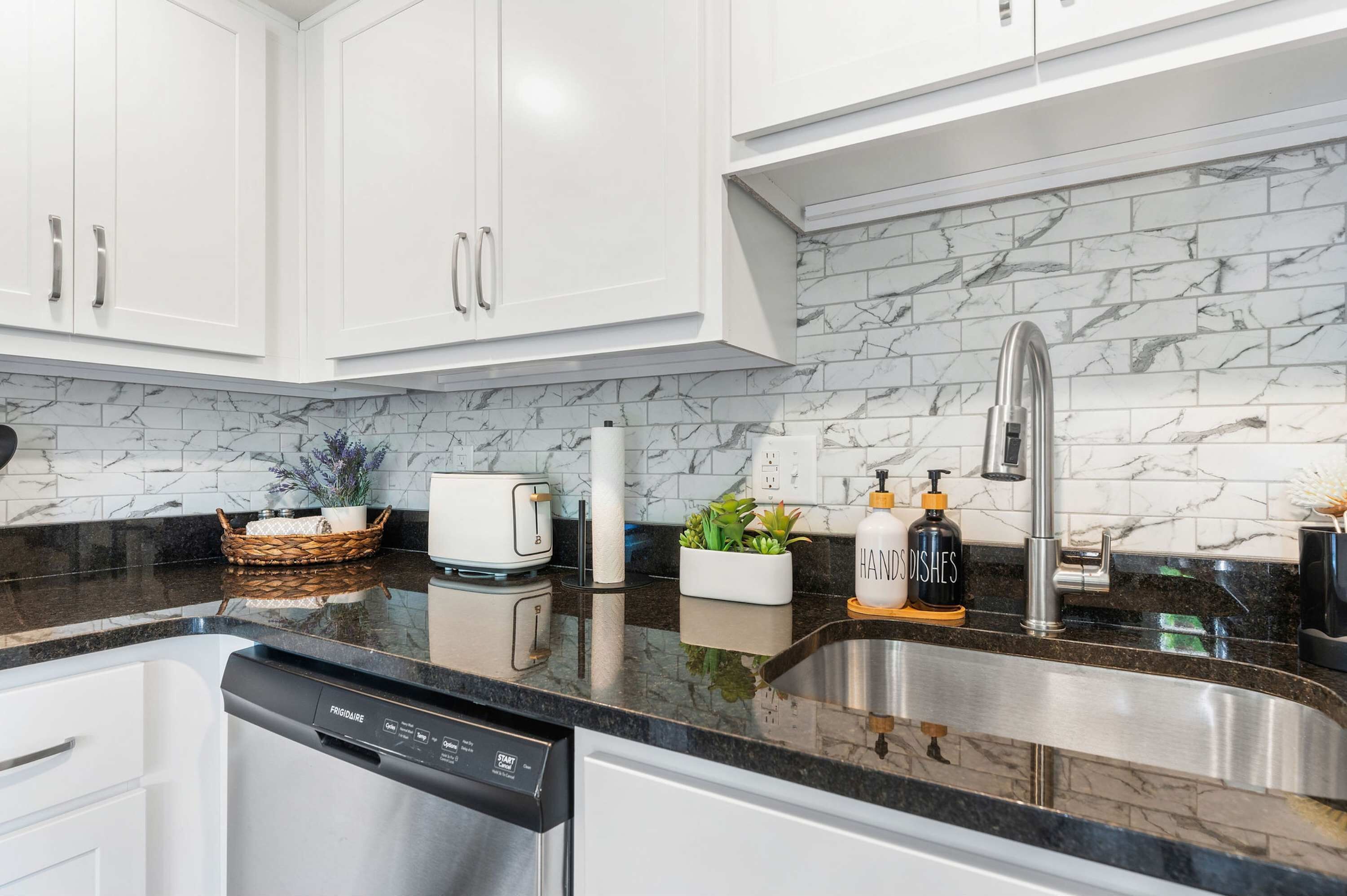 A modern kitchen with white cabinets, a marble backsplash, a stainless steel sink, and a dishwasher.