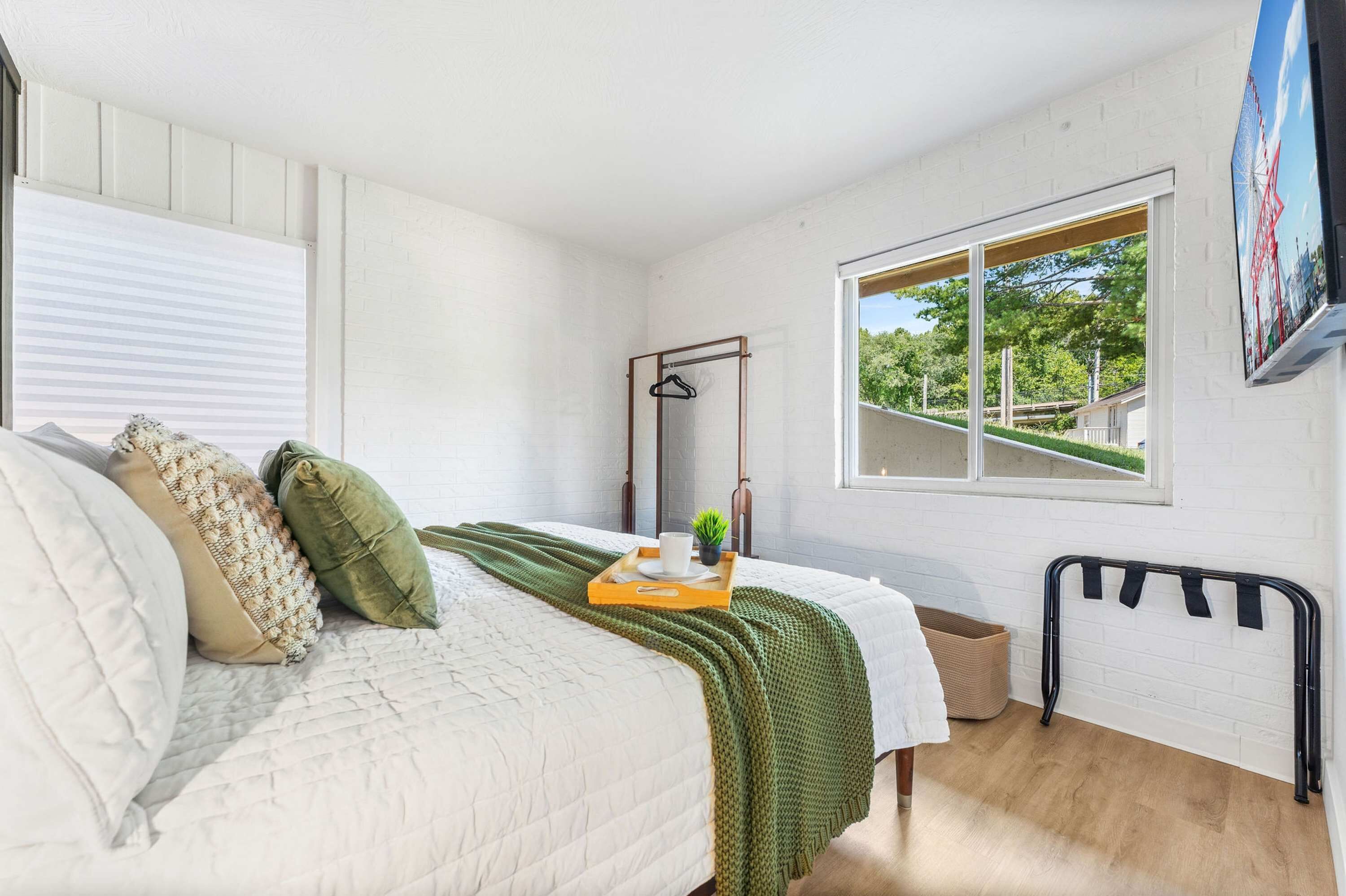 A bedroom with a bed, a window with a view, a hanging clothes rack, and a small plant on the bedside table.