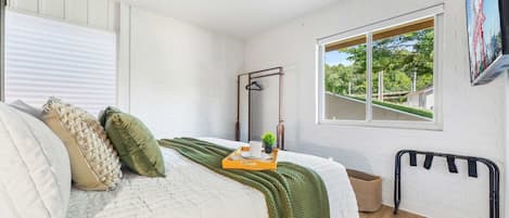 A bedroom with a bed, a window with a view, a hanging clothes rack, and a small plant on the bedside table.