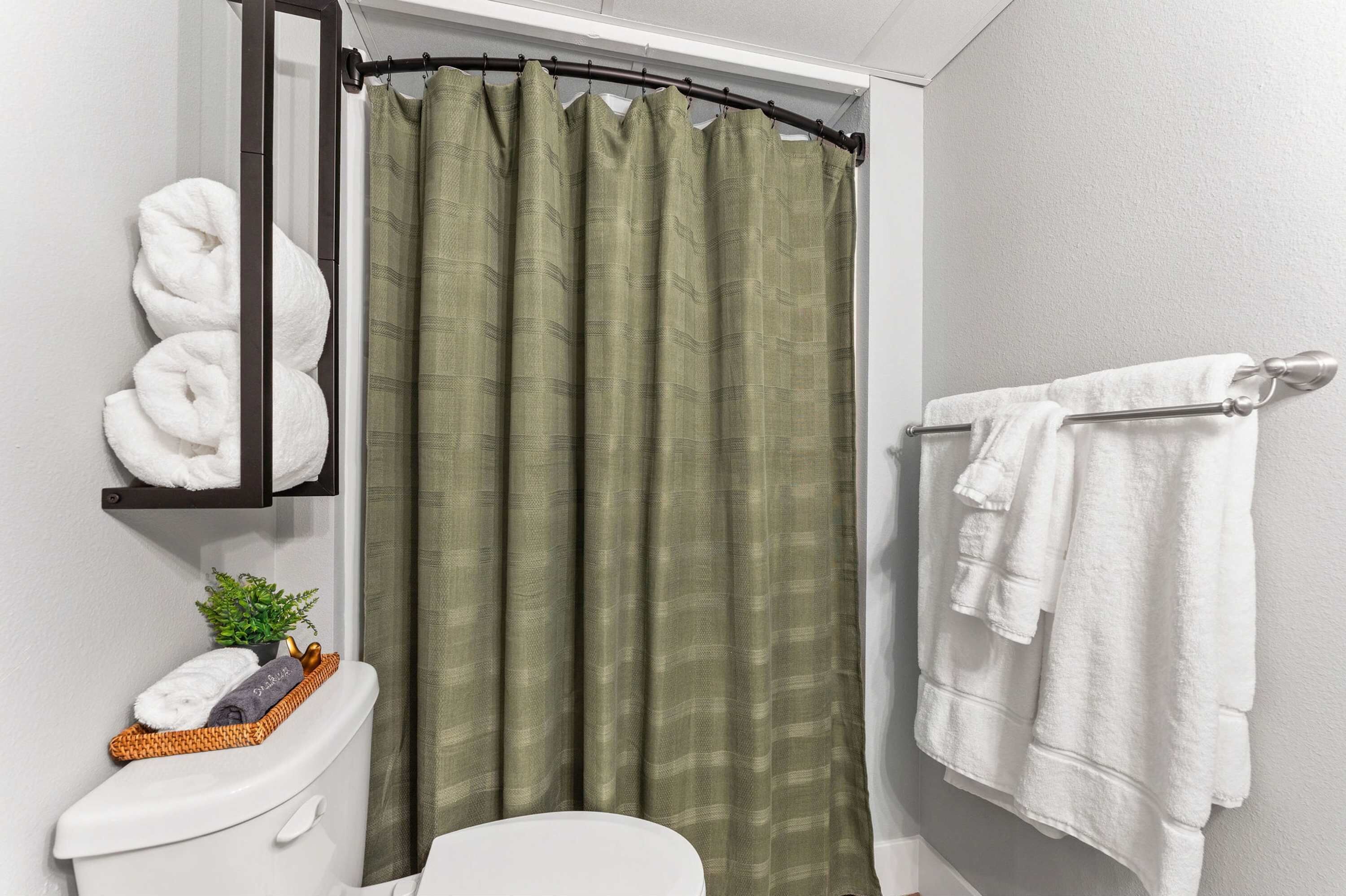 A bathroom with a toilet, a shelf with towels, a shower curtain, and a towel rack.