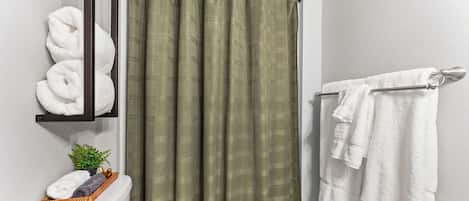A bathroom with a toilet, a shelf with towels, a shower curtain, and a towel rack.