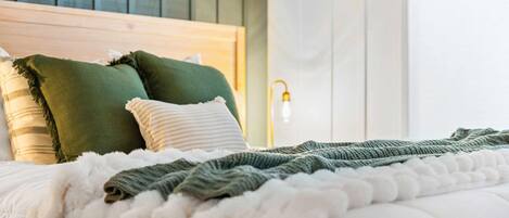 Een net opgemaakt bed met een witte dekbedovertrek, een kussen met groene en witte strepen, en een groene plaid.