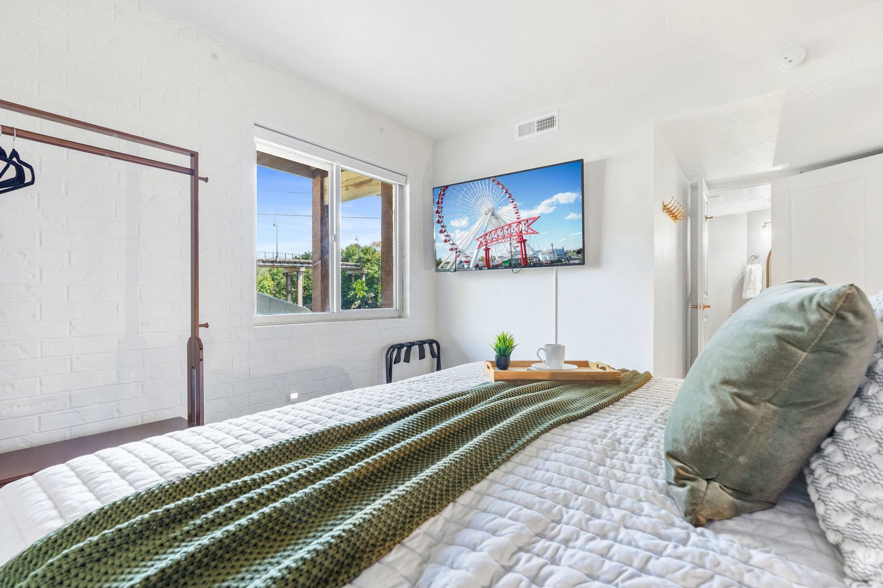 Une chambre à coucher avec un lit, une fenêtre, un téléviseur fixé au mur et une porte.