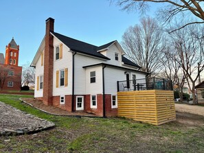 A two-story house with a brick facade and white siding, a chimney, and a wooden deck. - Charming Carolina Cottage in Downtown Mocksville (Mocksville)