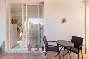 Un patio con una mesa y sillas, un muro cortinero que da a un espacio interior, y un adorno pequeño en la pared.