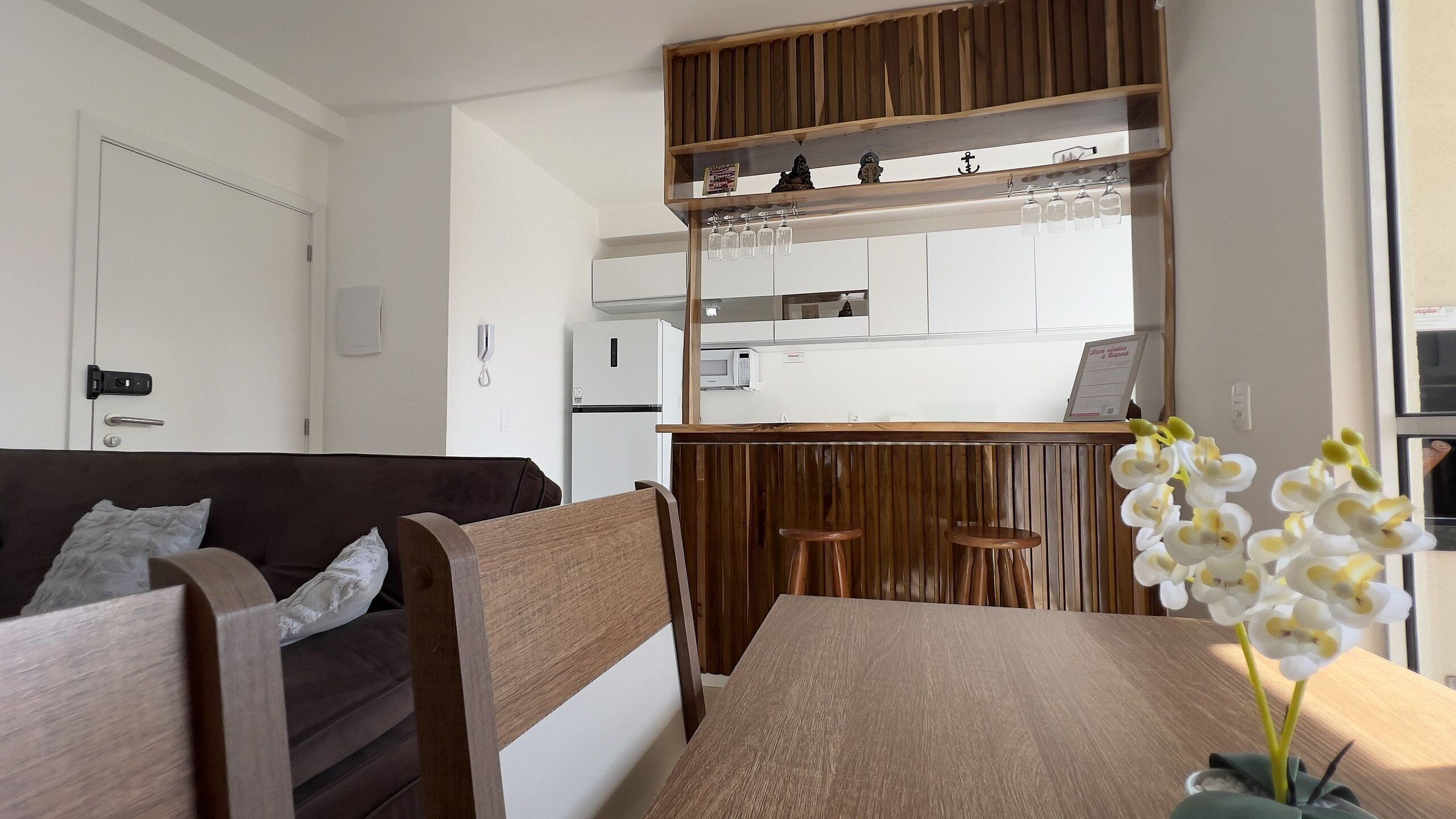 A modern living room with a wooden dining table, a sofa, and a kitchen in the background.