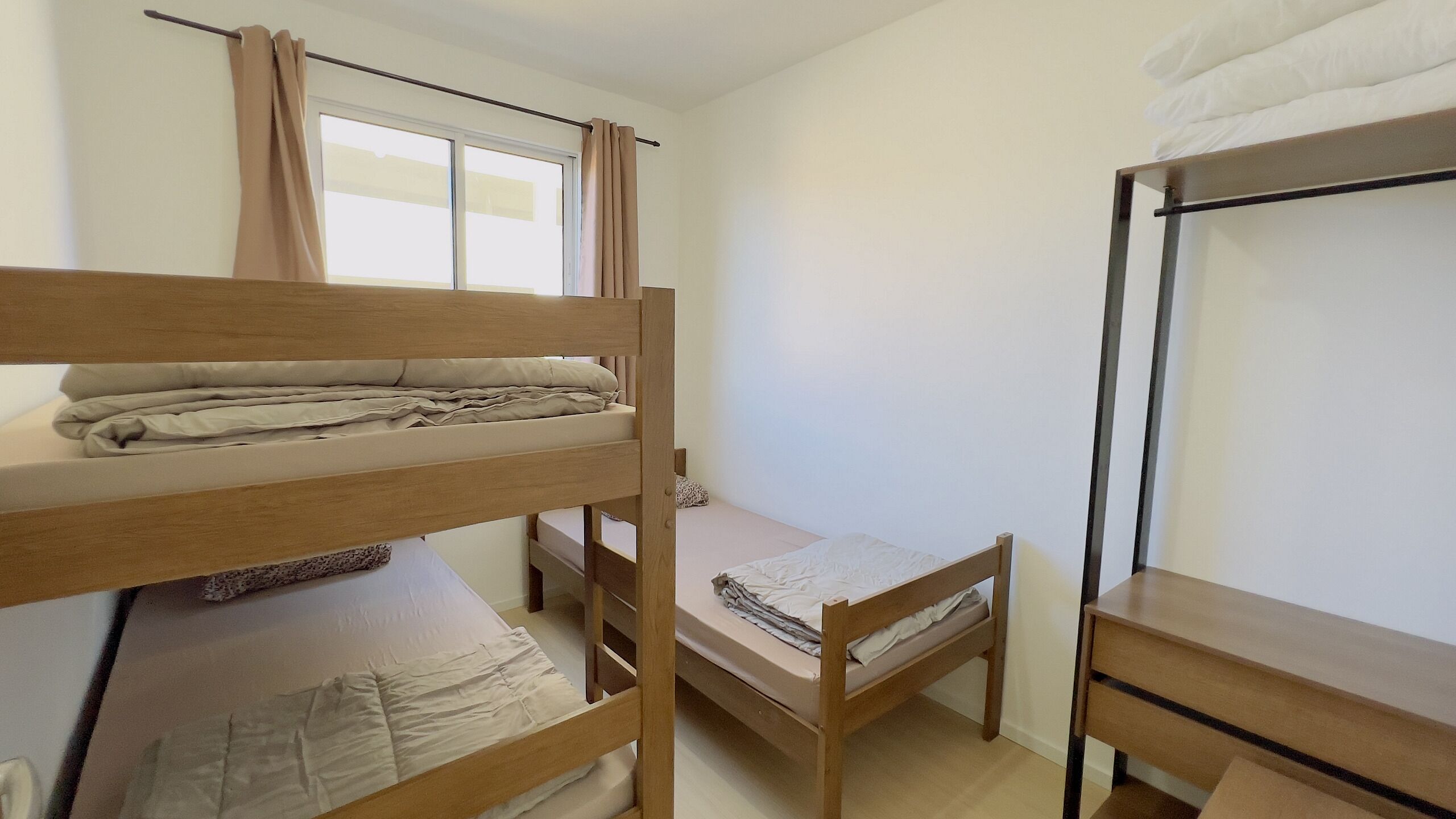 A dormitory room with bunk beds, a window with curtains, and a wooden desk.