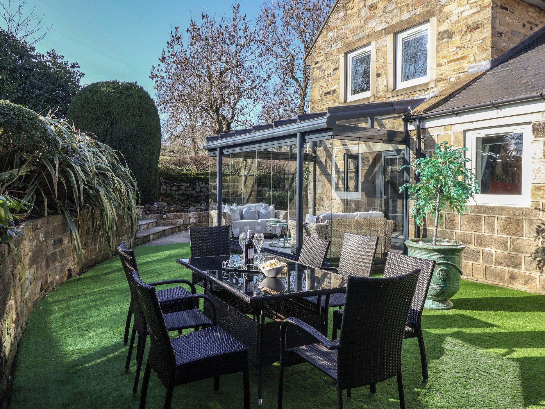 An outdoor patio with a glass enclosure, wicker furniture, and a stone building in the background.