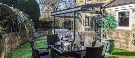 An outdoor patio with a glass enclosure, wicker furniture, and a stone building in the background.