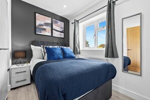 Un dormitorio moderno con una cama grande, una mesita de noche y una ventana con cortinas.