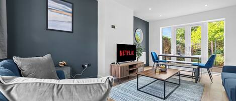 A modern living room with a dark grey wall, a large window, a flat-screen TV, a coffee table, and a blue sofa.