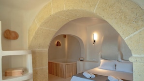 A modern, minimalist room with a stone archway, a wooden bathtub, and a neatly made bed with towels. - Cypresses Villas (South Pelion)