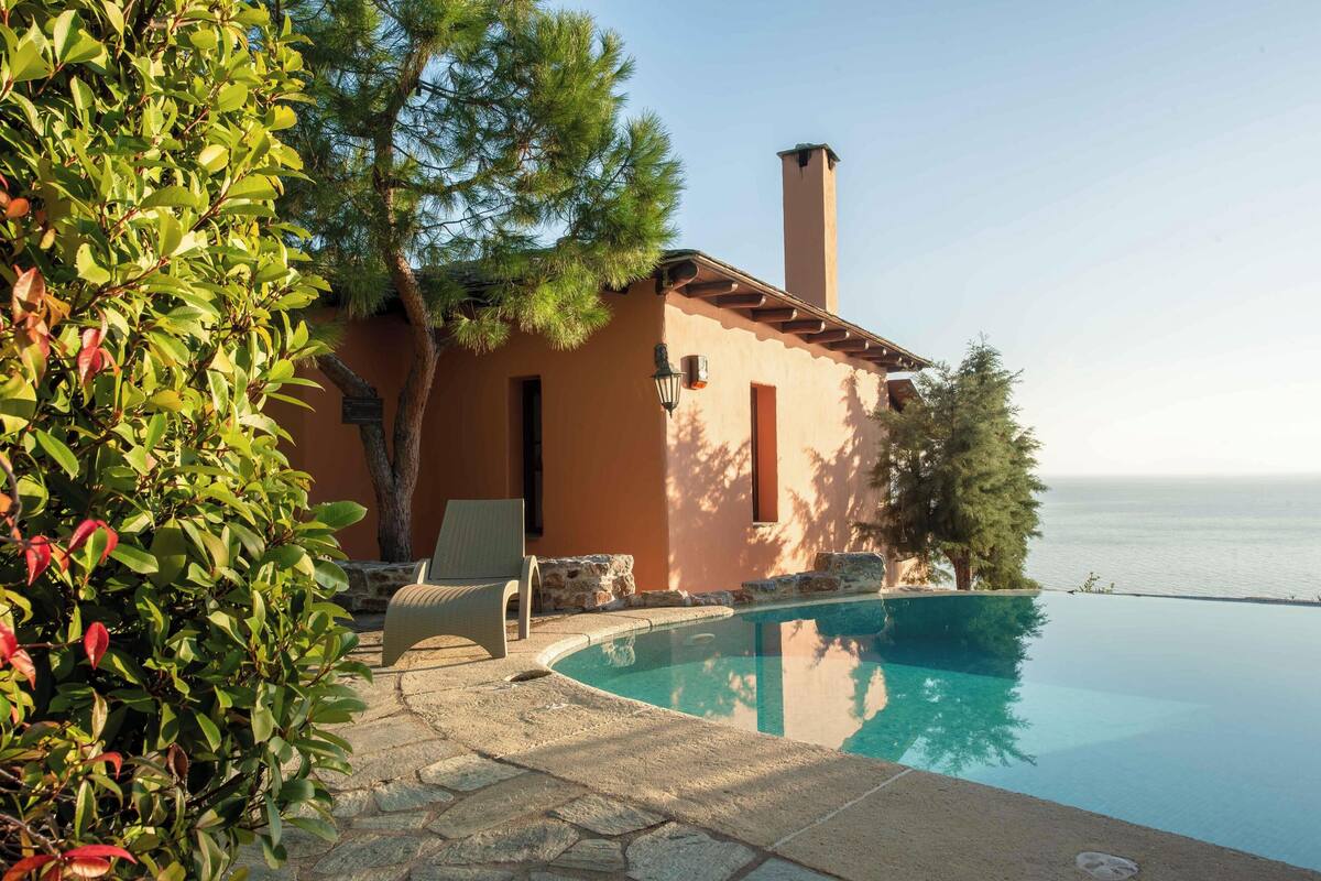A poolside area with a stone patio, a lounge chair, and a view of the sea.