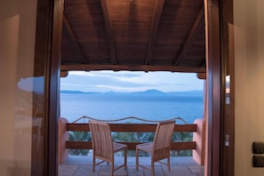 Un balcone in legno con due sedie rivolto verso un panorama mozzafiato tra mare e montagne.