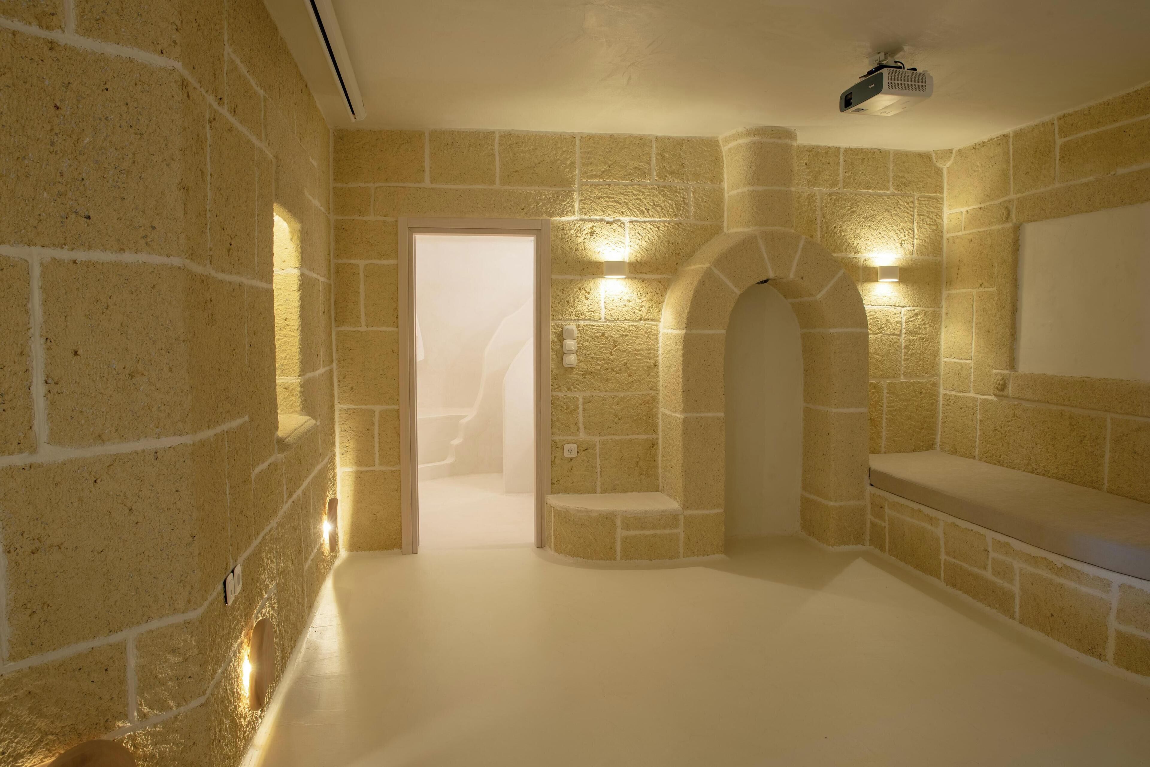 A stone-walled room with a white floor, a door, and a bench.