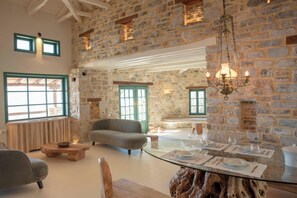 Un interior rústico de piedra con un sofá, una mesa de comedor de cristal para cuatro comensales y una araña.