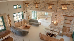 A spacious living area with a stone wall, a sofa, a glass dining table, and a hanging light fixture. - Cypresses Villas (South Pelion)