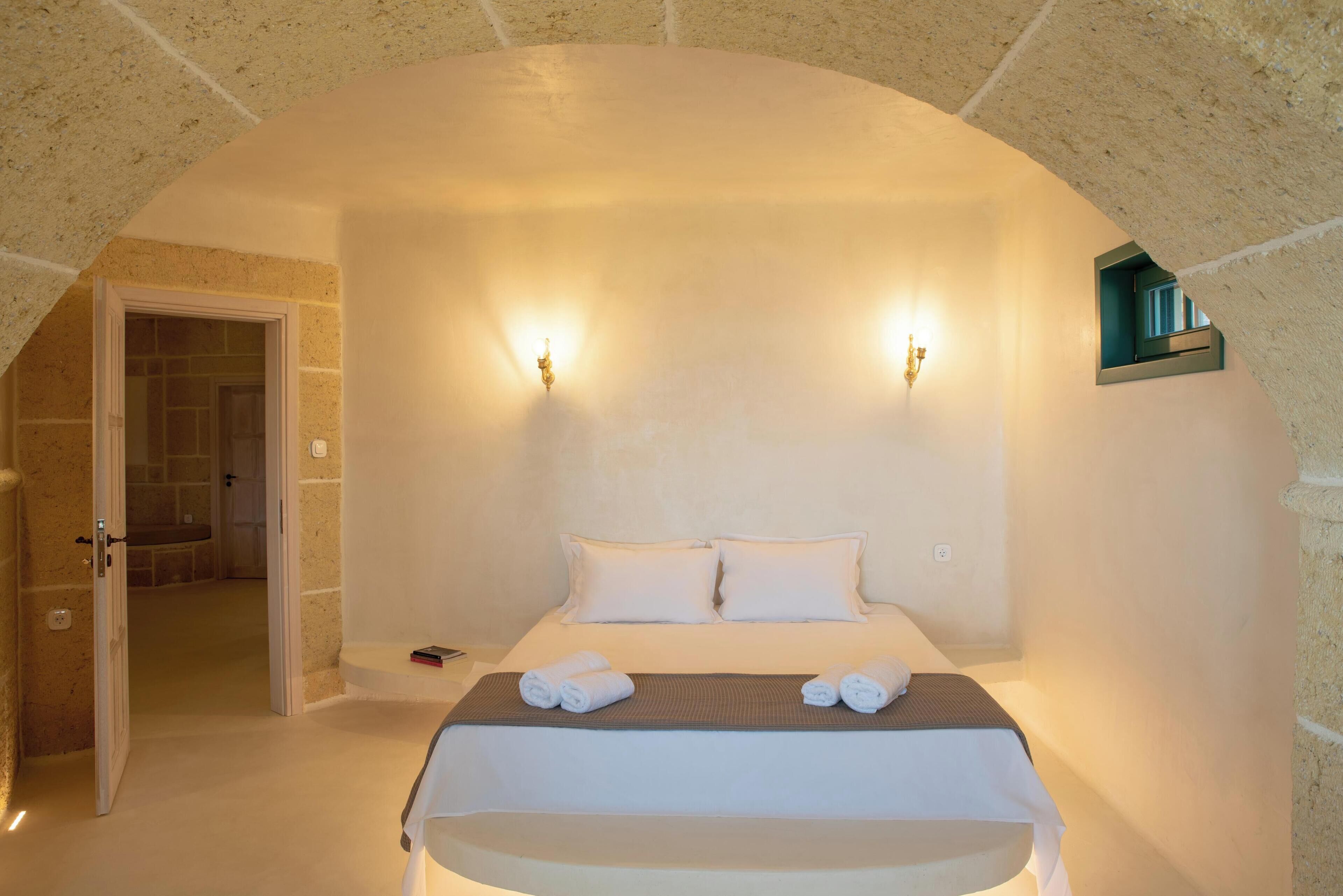 Un dormitorio con una cama grande, dos lámparas de pared y vistas a un baño a través de una puerta abierta.