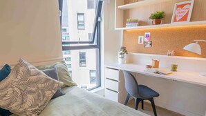 Een slaapkamer met een bed, een bureau en uitzicht op gebouwen door een raam.