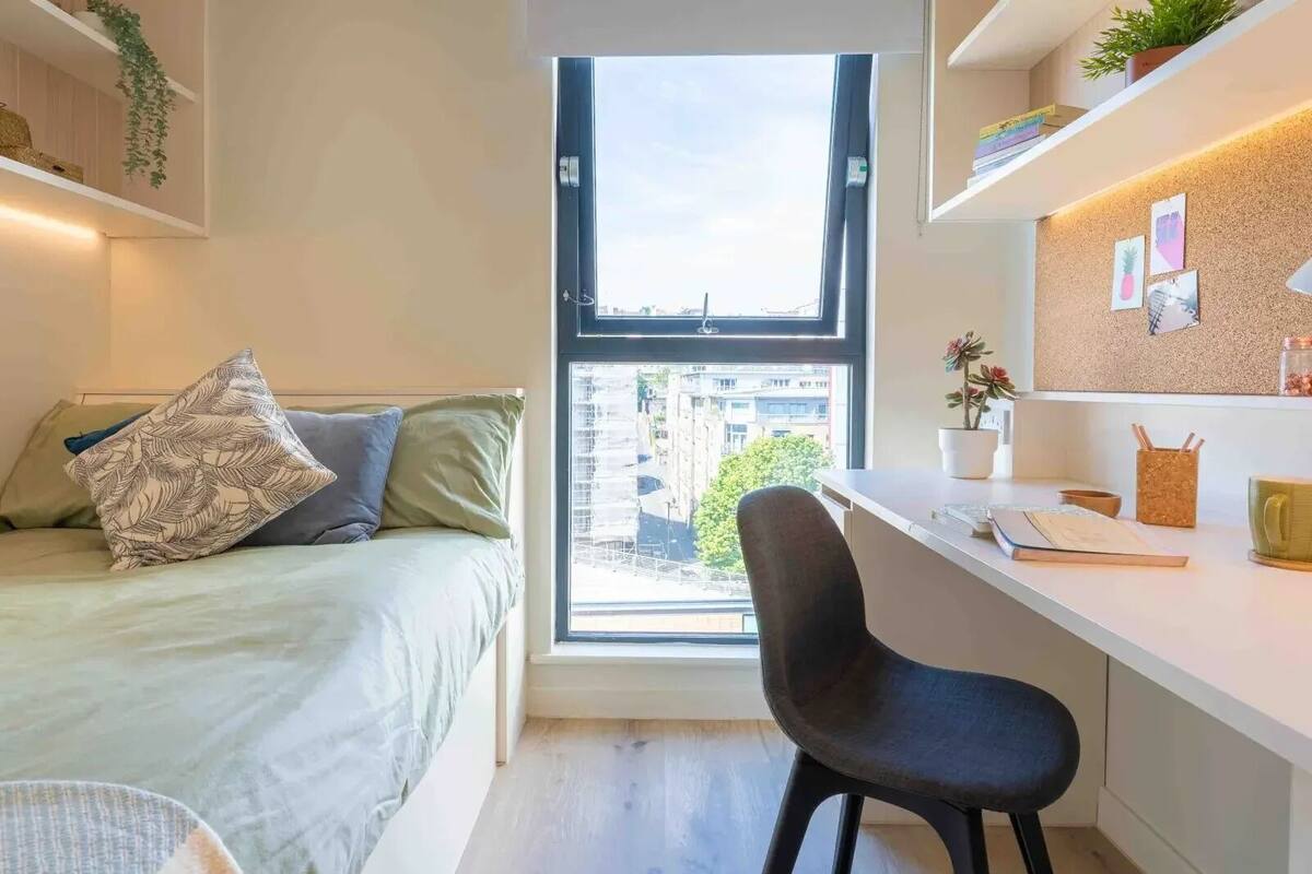 A bedroom with a bed, a desk, and a window.