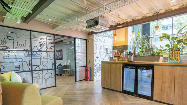 Een moderne kantoorruimte met een houten toonbank, een koelkast en een groene bank.