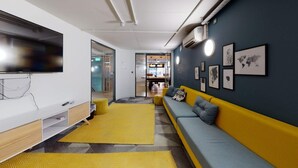 Een moderne woonkamer met een gele bank, een grote flatscreen televisie en een kamerkleed met een patroon.
