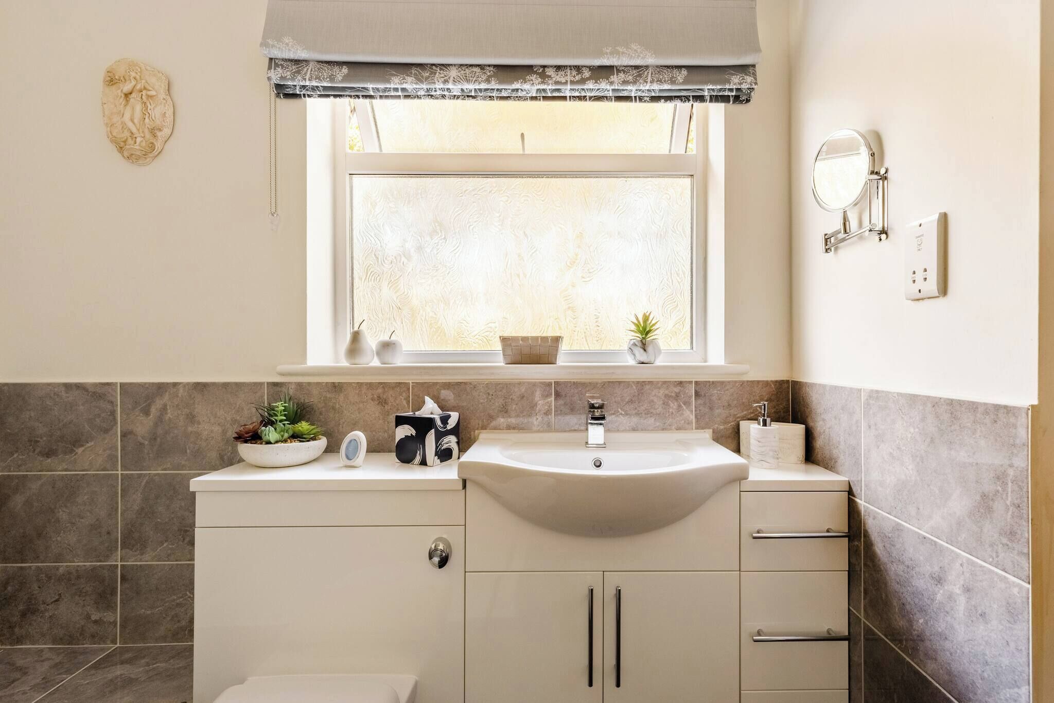 A bathroom with a white sink, a mirror, and a window above the sink.