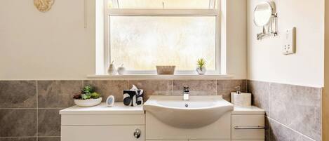 A bathroom with a white sink, a mirror, and a window above the sink.