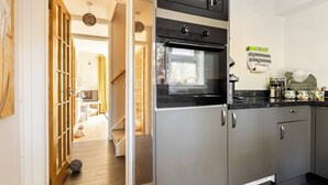 A modern kitchen with a built-in oven and microwave, a wooden door leading to a living area, and a countertop with kitchen essentials. - Cosy Annex, South Facing Patio (Falmouth)