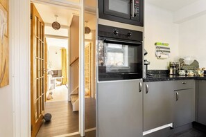 A modern kitchen with a built-in oven and microwave, a wooden door leading to a living area, and a countertop with kitchen essentials. - Cosy Annex, South Facing Patio (Falmouth)
