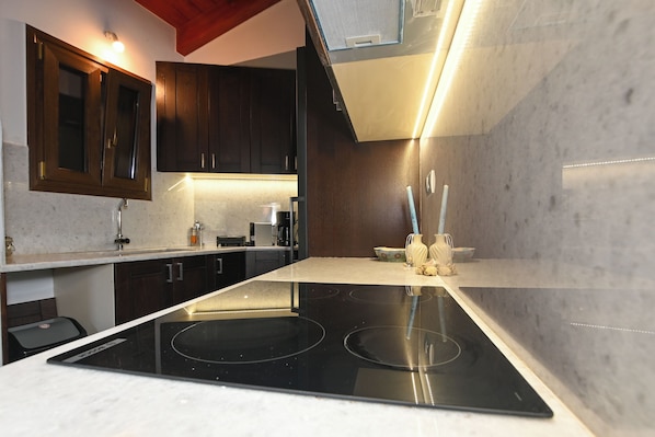 A modern kitchen with dark wooden cabinets, a black induction cooktop, and a marble countertop. - Chania Hillside 2BD Home – Nature & Comfort by ΜΡS (Plemeniana)