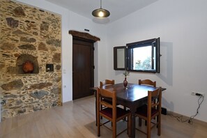 A dining area with a stone wall, wooden table, chairs, and a window. - Chania Hillside 2BD Home – Nature & Comfort by ΜΡS (Plemeniana)