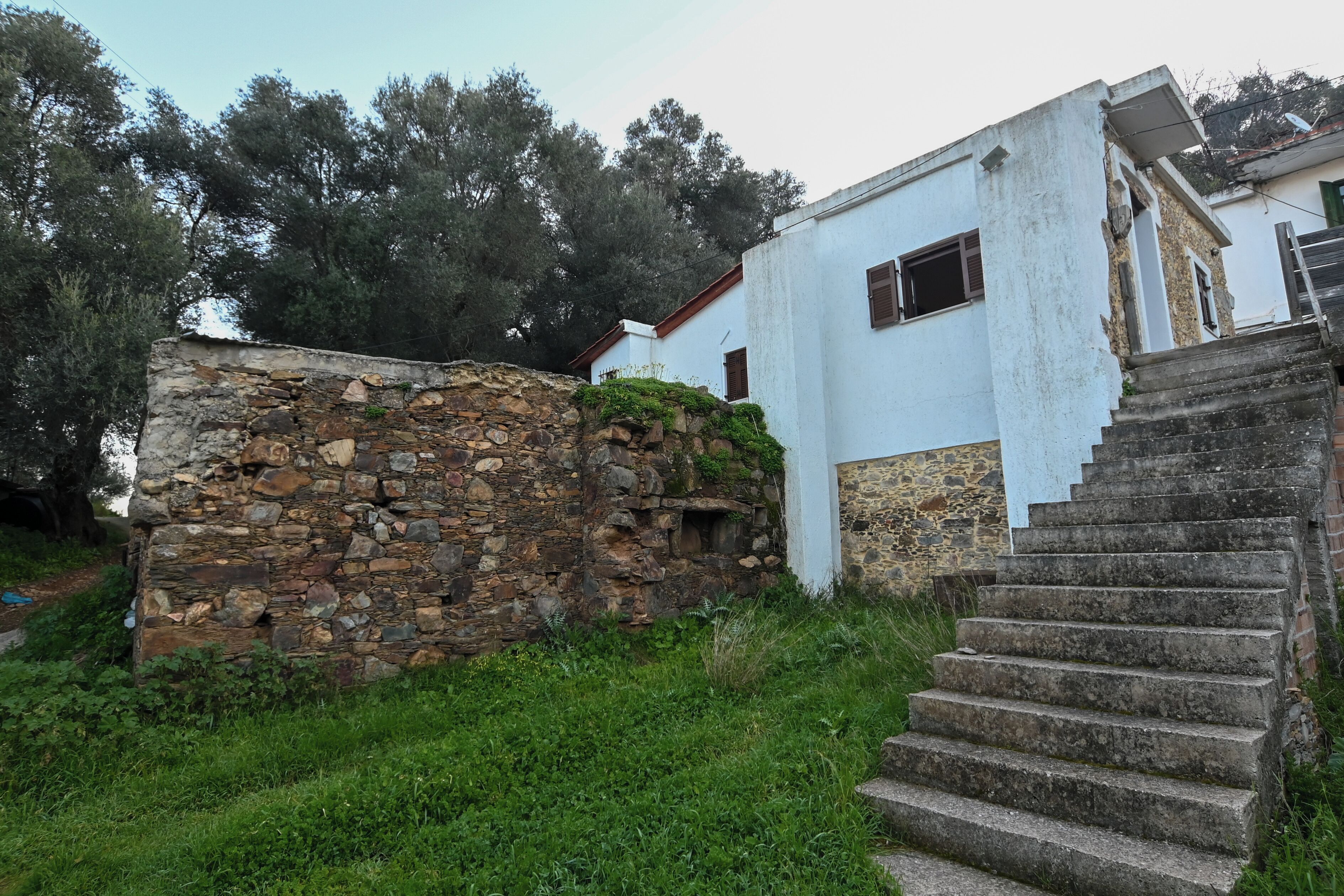 Paredede pedra ao lado de um edifício branco, com uma escadaria que leva a uma porta.