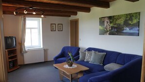 Een woonkamer met een blauwe bank, een houten salontafel en een schilderij van een watermolen aan de muur.