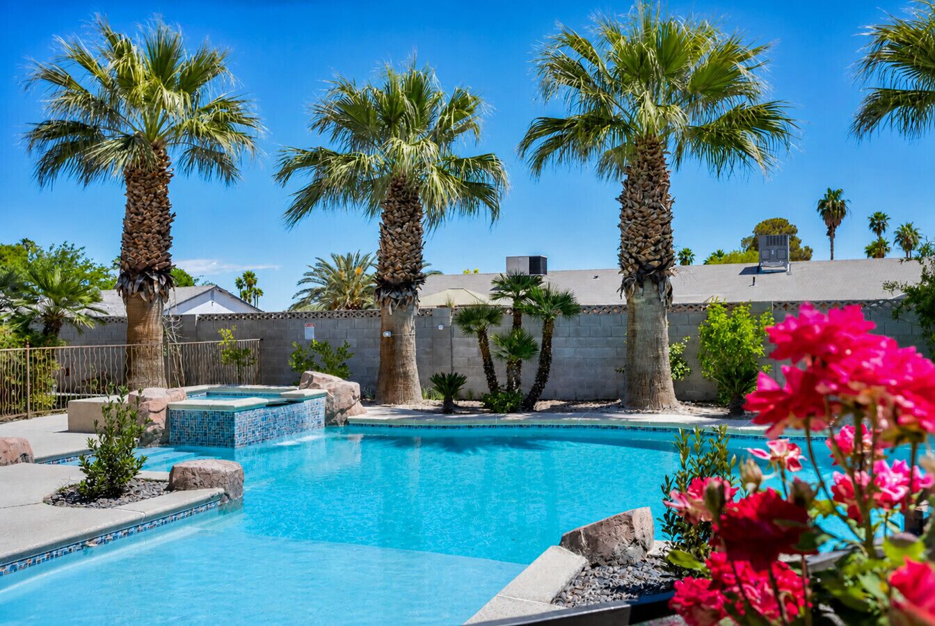 Una piscina con palmeras, un suelo de baldosas y una pared de piedra.
