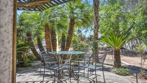 Eine Terrasse mit einem Glastisch und Metallstühlen, umgeben von Palmen und einer Pergola.
