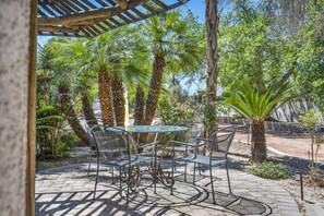 Eine Terrasse mit einem Glastisch und Metallstühlen, umgeben von Palmen und einer Pergola.