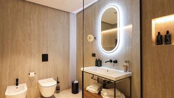 A modern bathroom with a bidet, toilet, vanity with a mirror, and a shelf with toiletries.