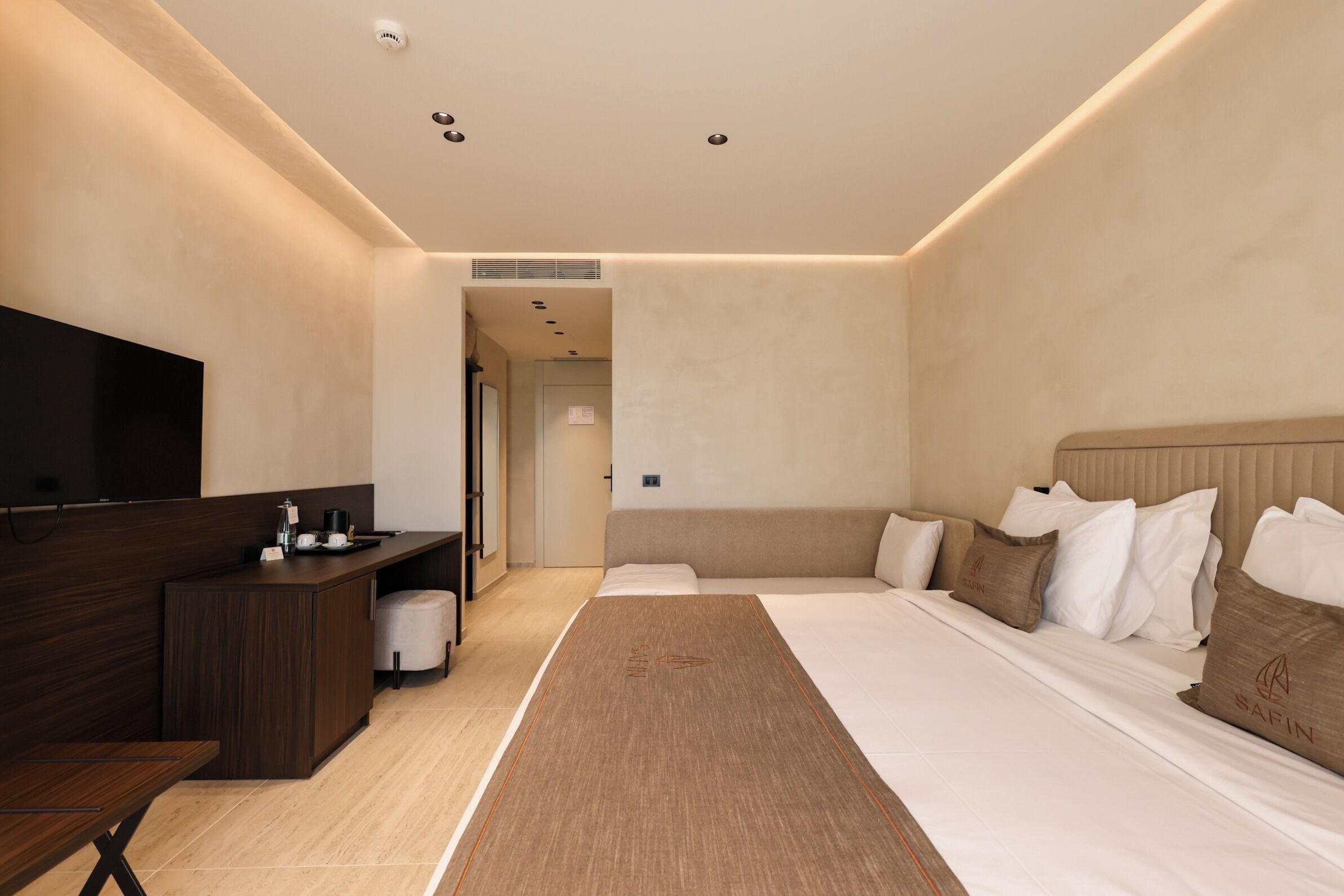 Ein modernes Hotelzimmer mit Bett, Schreibtisch, Fernseher und einem durch eine offene Tür einsehbaren Badezimmer.