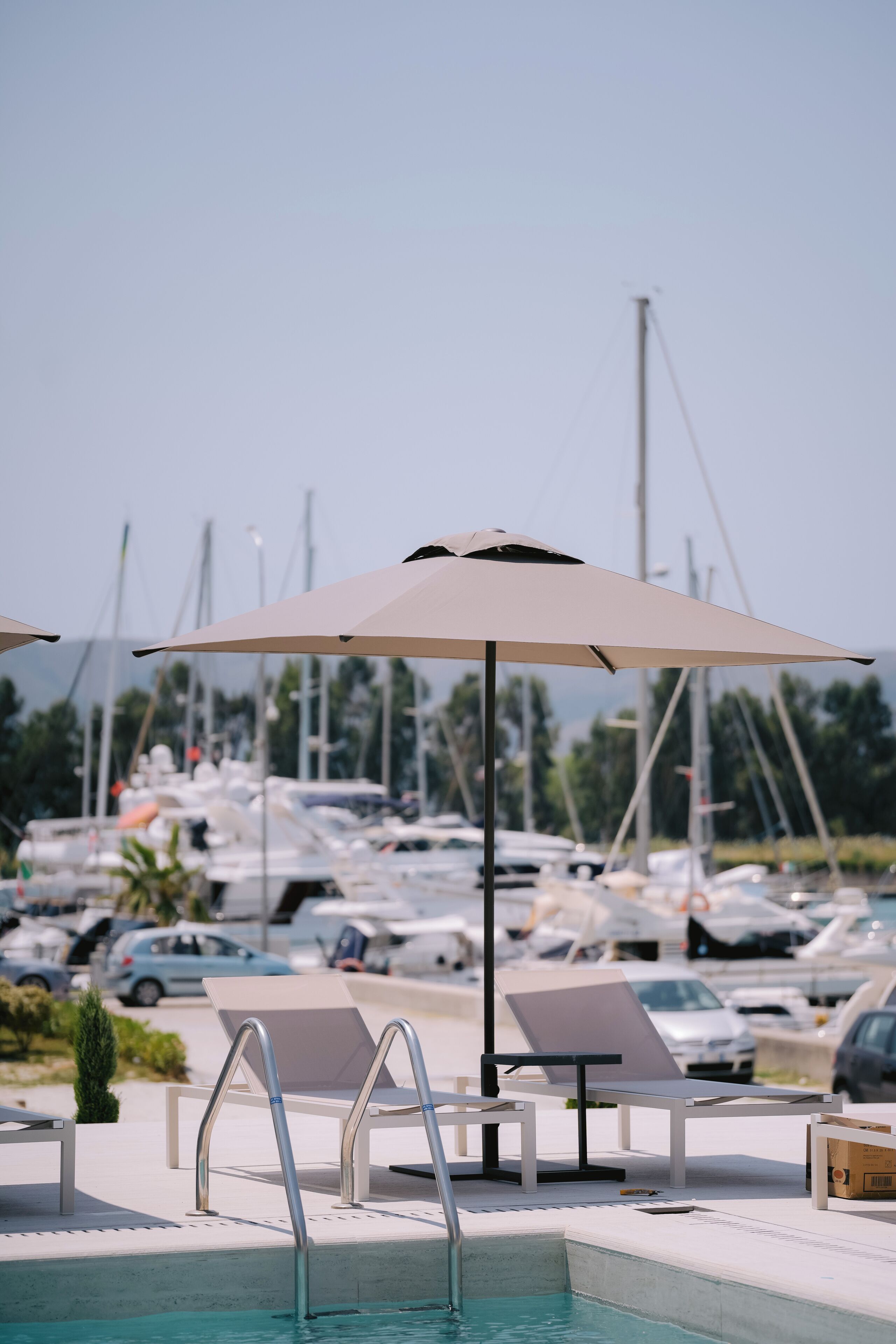 Zona de piscina con sillones reclinables, una piscina y un puerto deportivo al fondo.