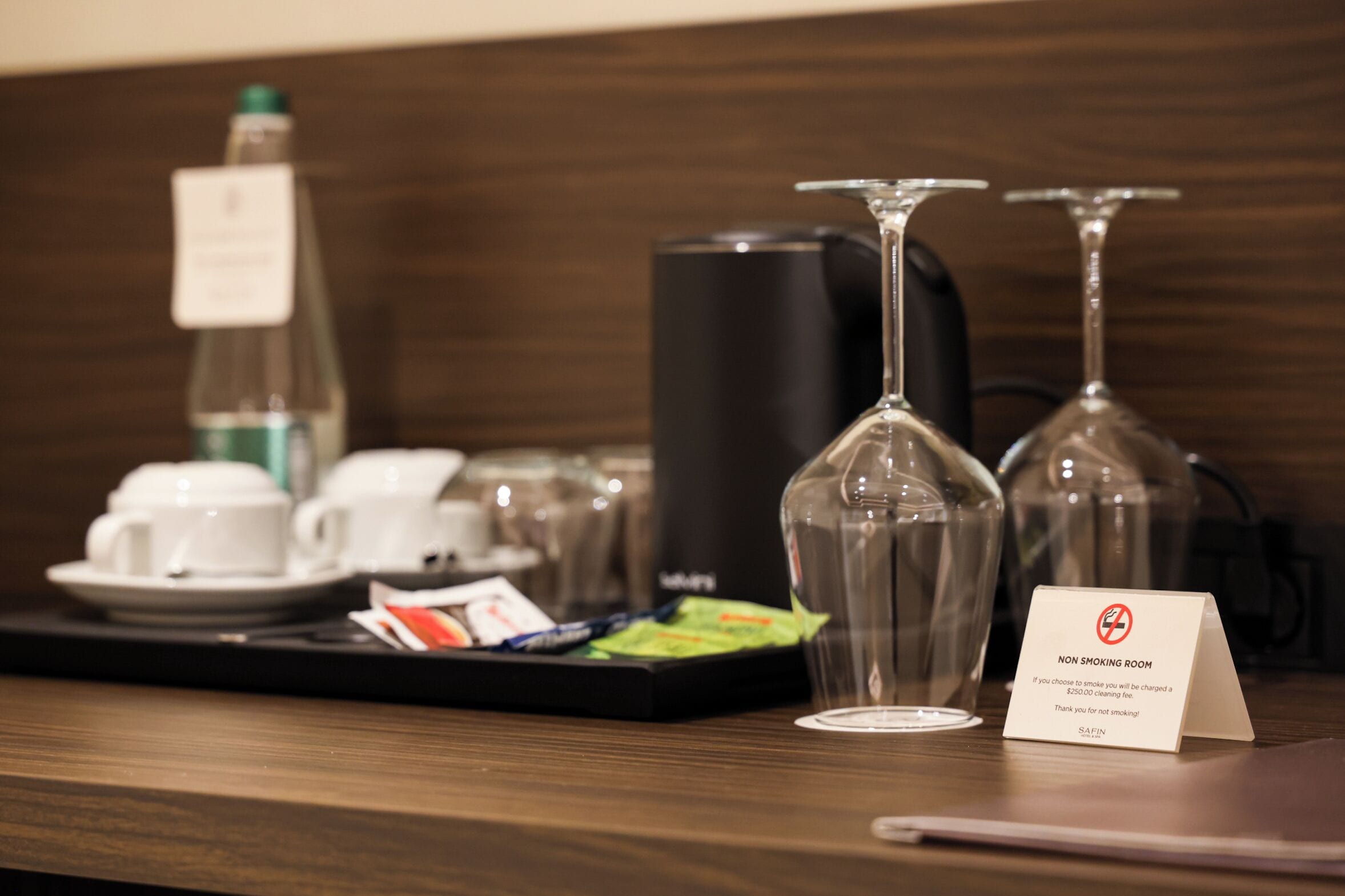 A hotel reception area with a coffee station, wine glasses, and a non-smoking sign.