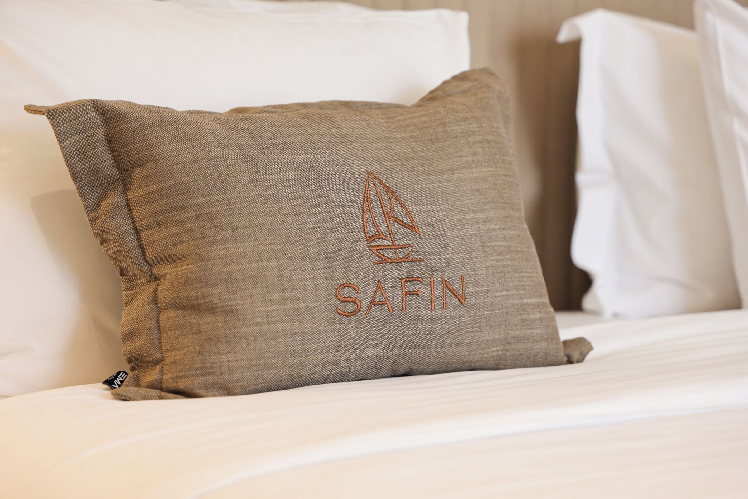 A bed with a pillow featuring a sailboat logo and the word 'SAFIN.'