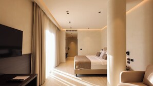 A modern hotel room with a bed, a TV, a sofa, and a large window with curtains. - Safin Hotel & SPA (Orikum)