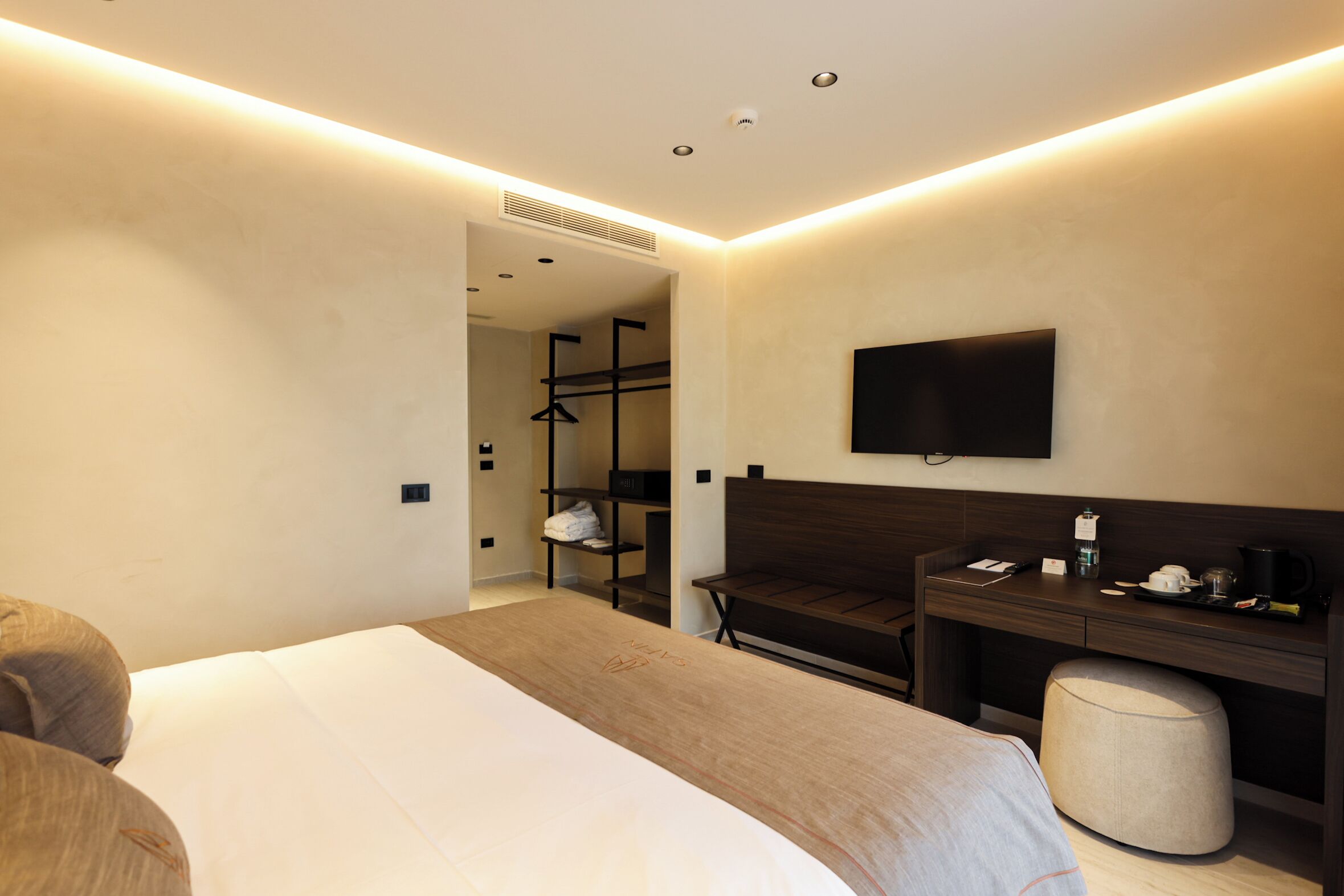 Ein modernes Hotelzimmer mit einem großen Bett, einem Schreibtisch mit Stuhl, einem an der Wand befestigten Fernseher und einem begehbaren Kleiderschrank.