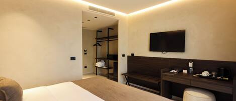 Ein modernes Hotelzimmer mit einem großen Bett, einem Schreibtisch mit Stuhl, einem an der Wand befestigten Fernseher und einem begehbaren Kleiderschrank.